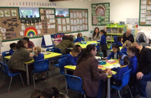 Parent-child reading session during school hours at Roger Ascham Primary, with several adults and children in blue uniforms engaged with books.